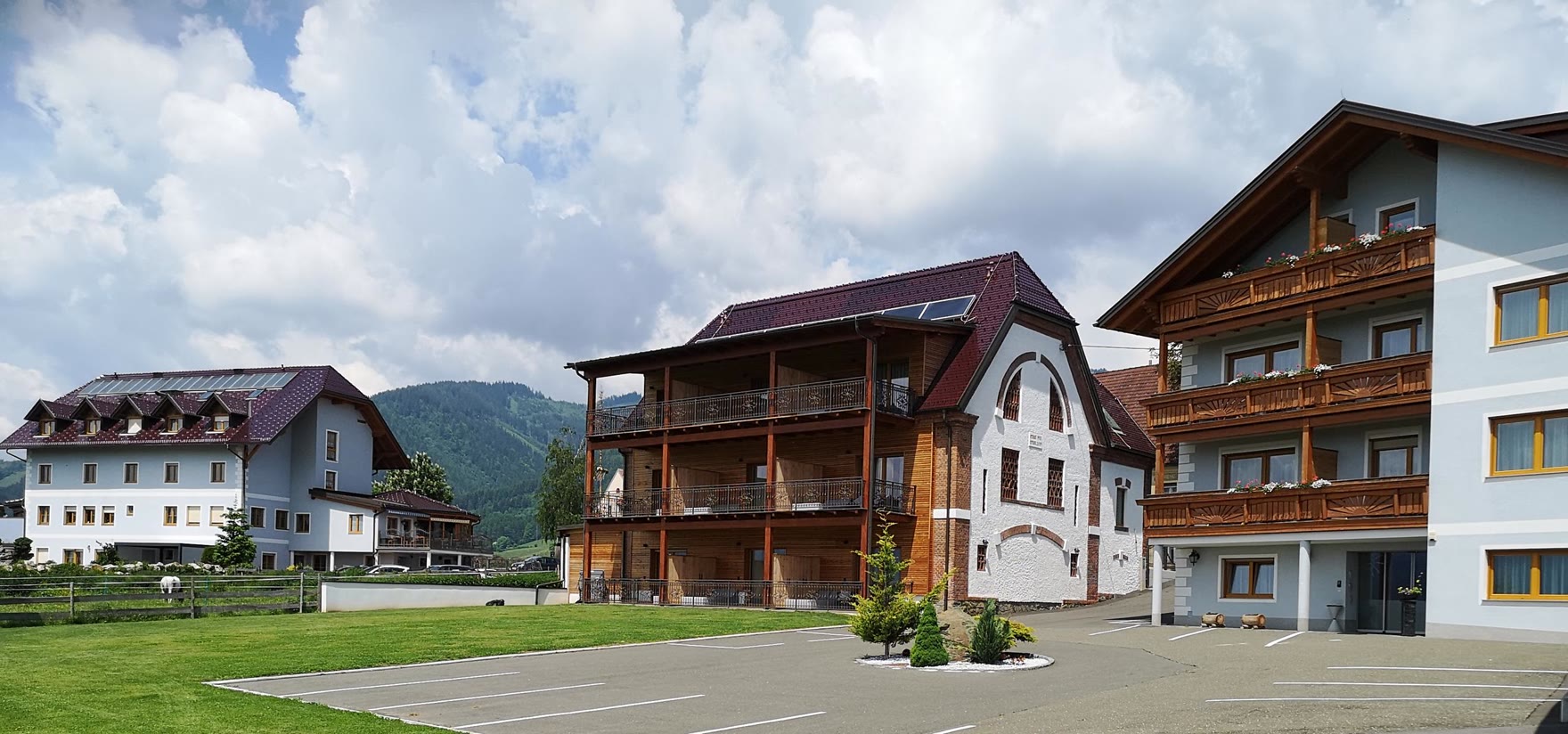 Stammhaus, Stadl und Chalet nebeneinander, dahinter die Berge des Murtals